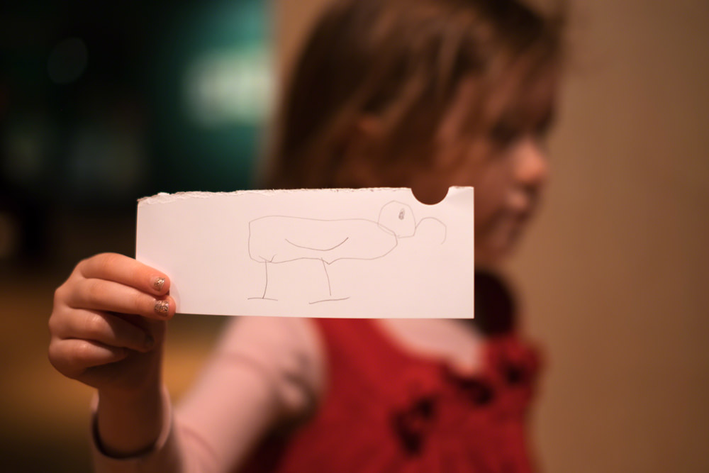 A young girl holds out a piece of paper with an ibis drawn on it