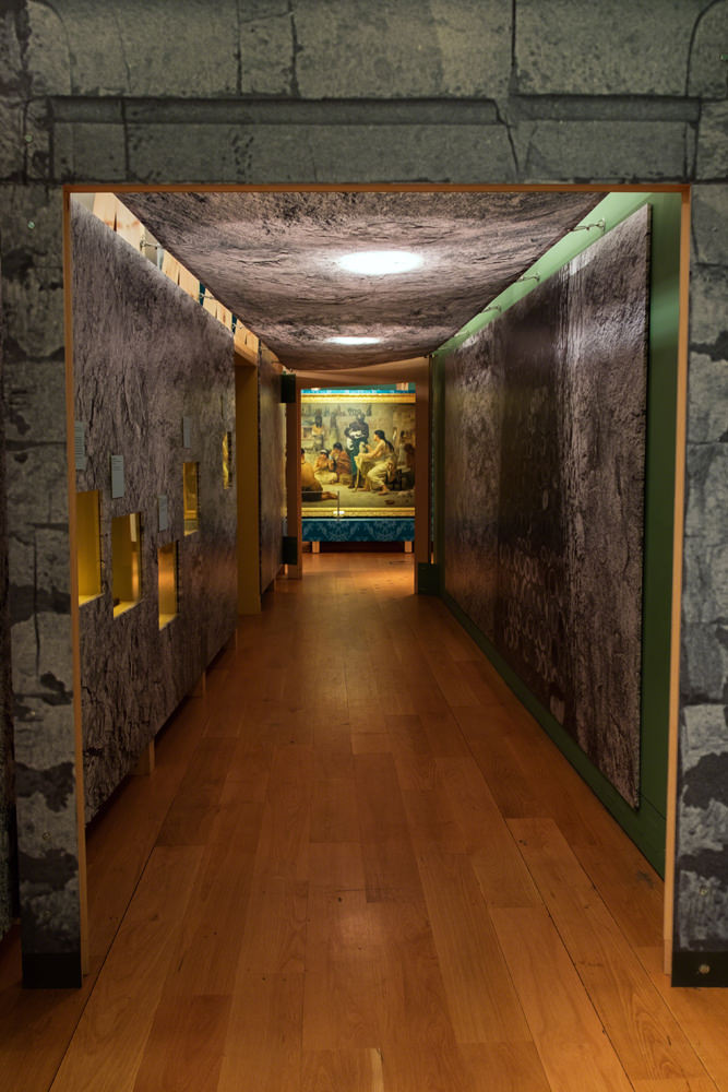 A reproduction of a catacomb tunnel, with stone-like walls and a large 19th century painting at the other end