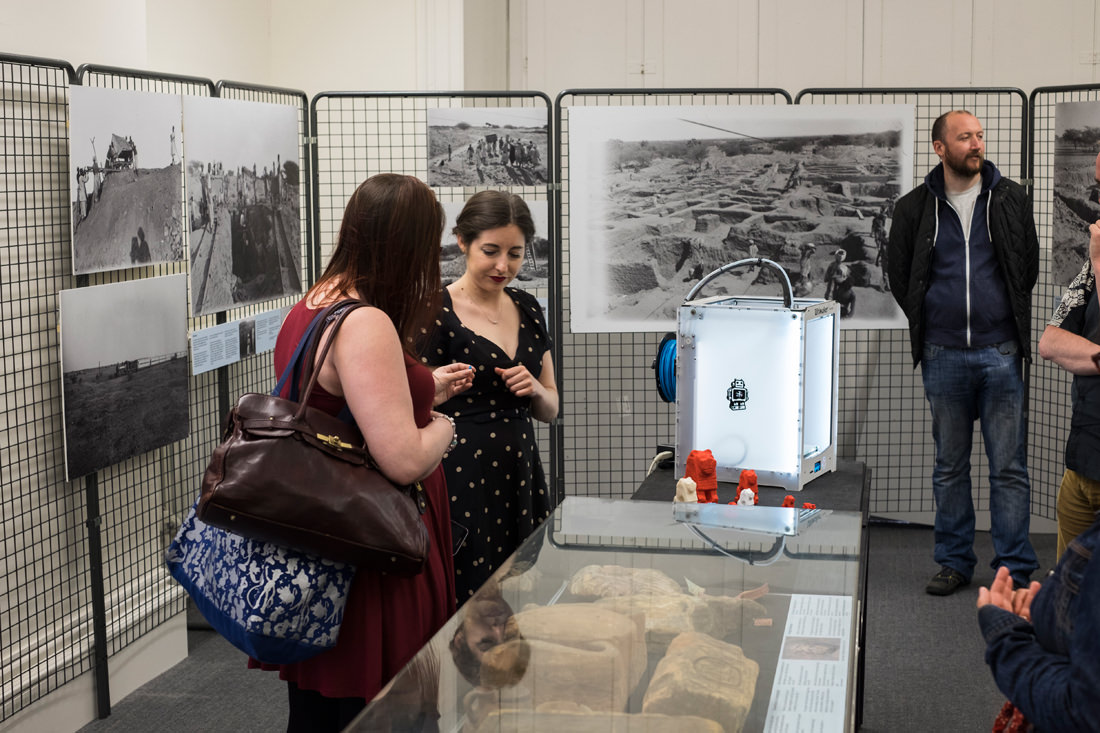 Looking at the back half of the exhibition room. There are a few people in there. Next to the display case are two women looking at the 3D printed lion statues