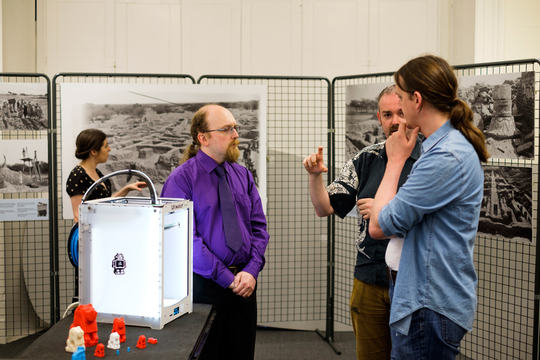 Three men standing next to the 3D printer, talking