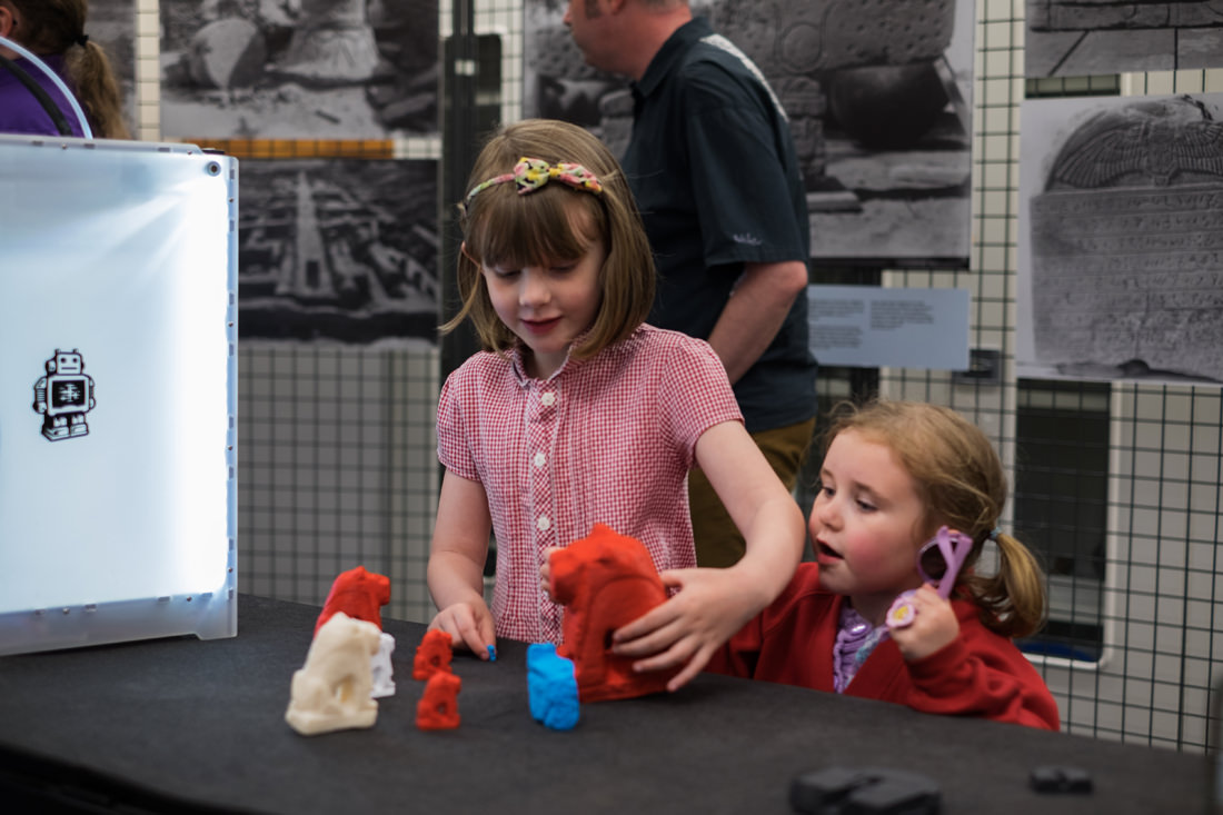 Two young girls, in school uniform, standing next to the table and playing with the 3D-printed lion statues