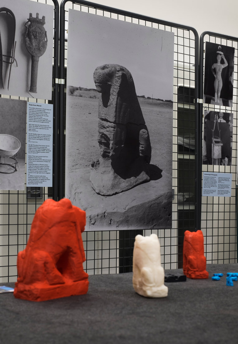 Three of the larger 3D printed lions are facing away from the camera, looking towards one of the photos, which is of a large stone statue of a lion