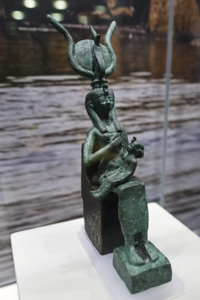 A statue of the Egyptian goddess Isis seated on a throne, nursing the child Horus