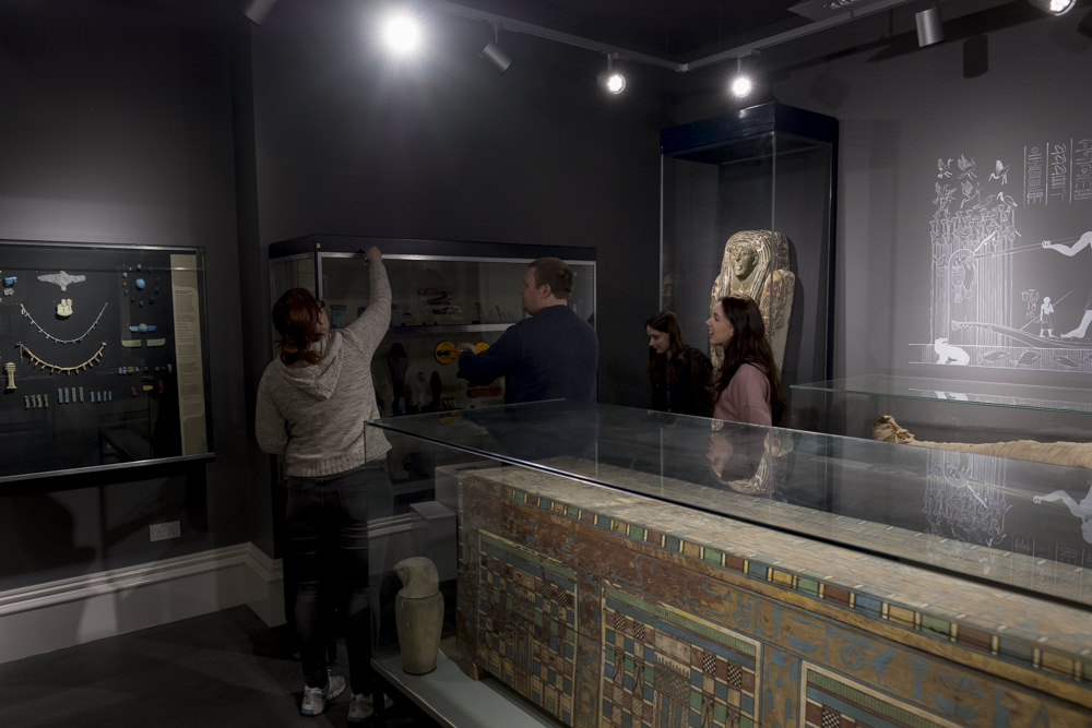 Four people in a museum gallery removing the glass from the front of a display case