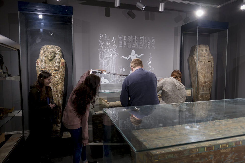 Four people in a museum gallery removing the glass from the front of a display case