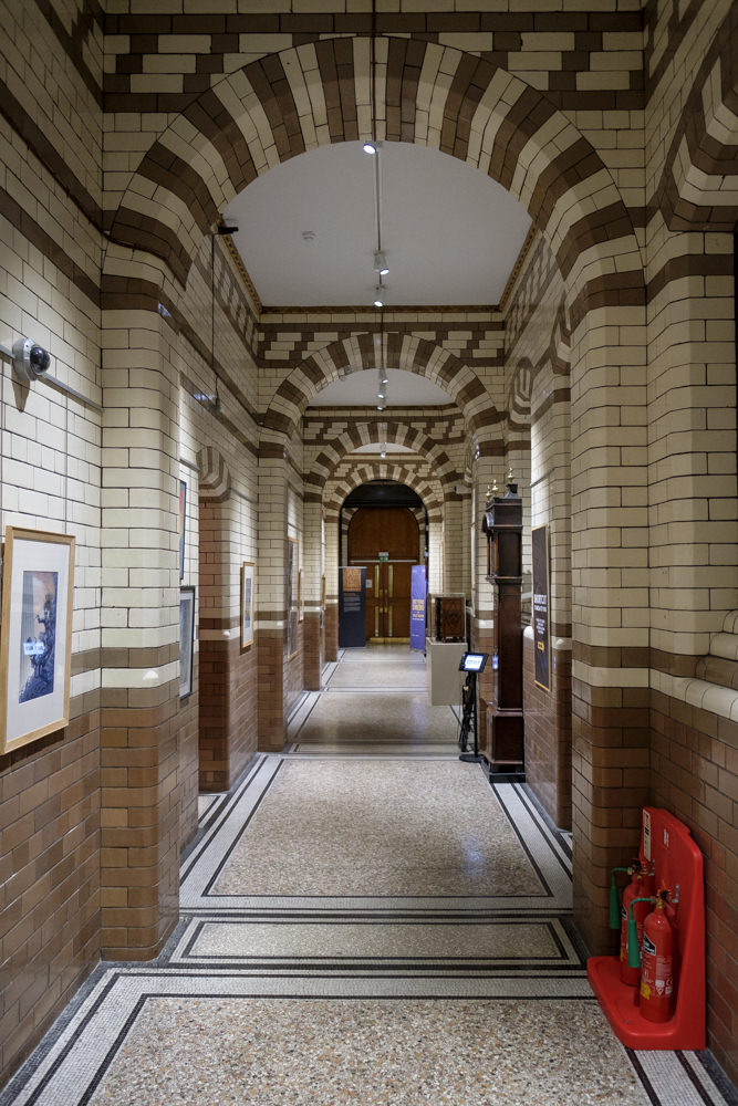 Looking down a long, straight hallway tiled in Victorian-era tiling