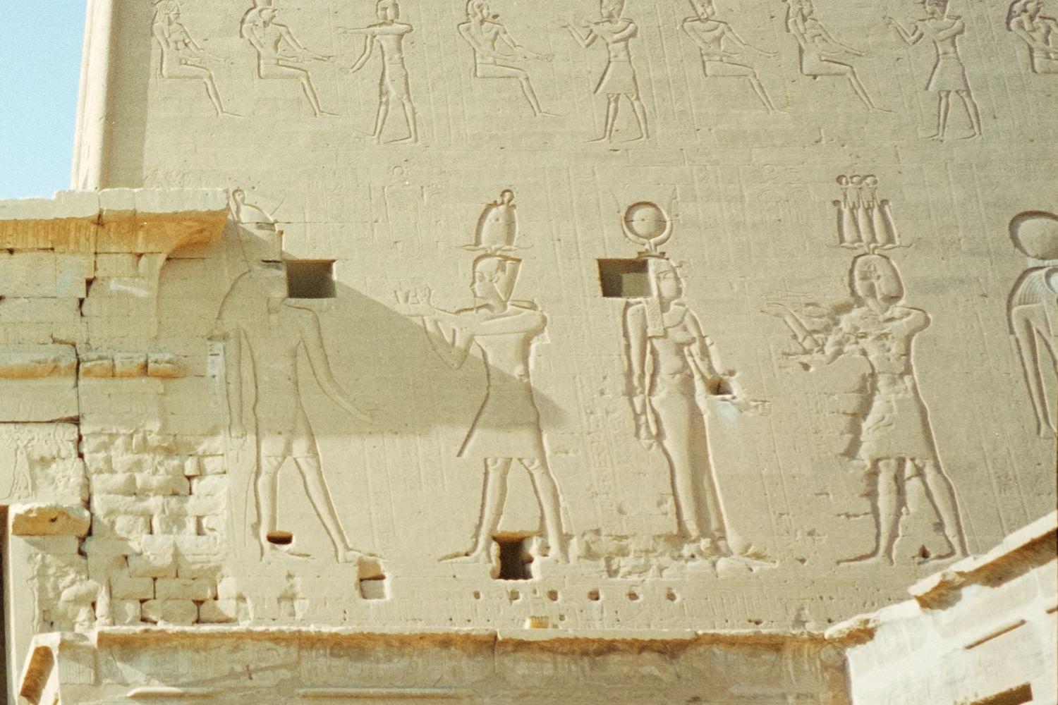 A close-up of carvings on the walls of Edfu temple showing various deities and pharaohs, including Isis