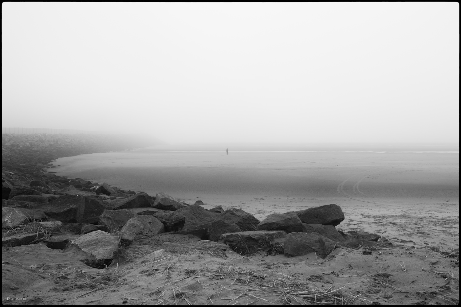 the approach to crosby beach on a foggy day with rocks in the foreground