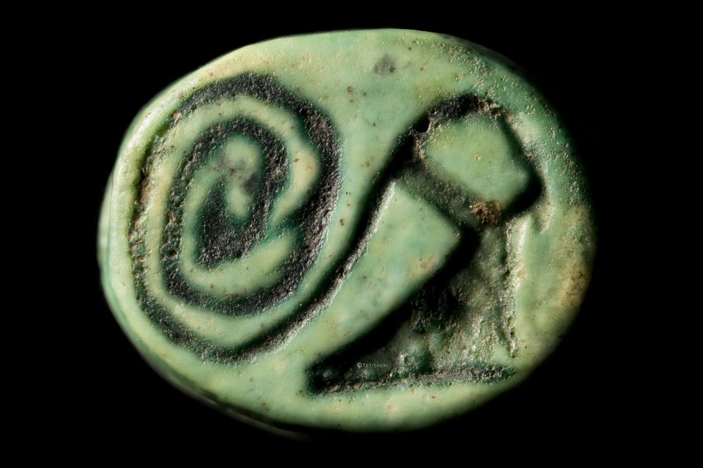 a small, green scarab with a spiral and a seated falcon with sundisk headdress