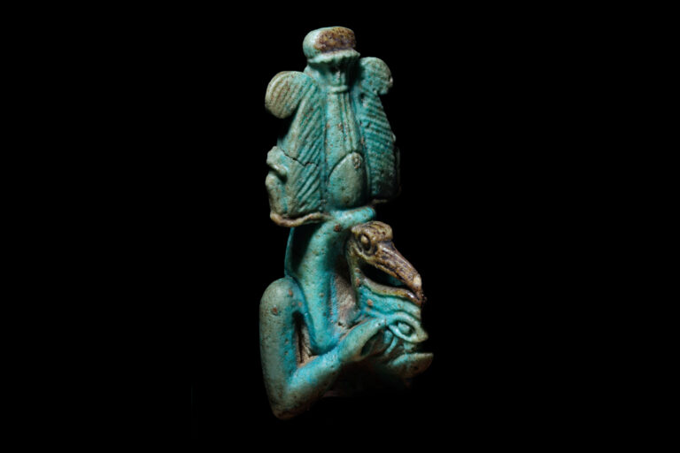 The photo showing the amulet from a front quarter-profile view, making the face, crown, eye and hands all visible.