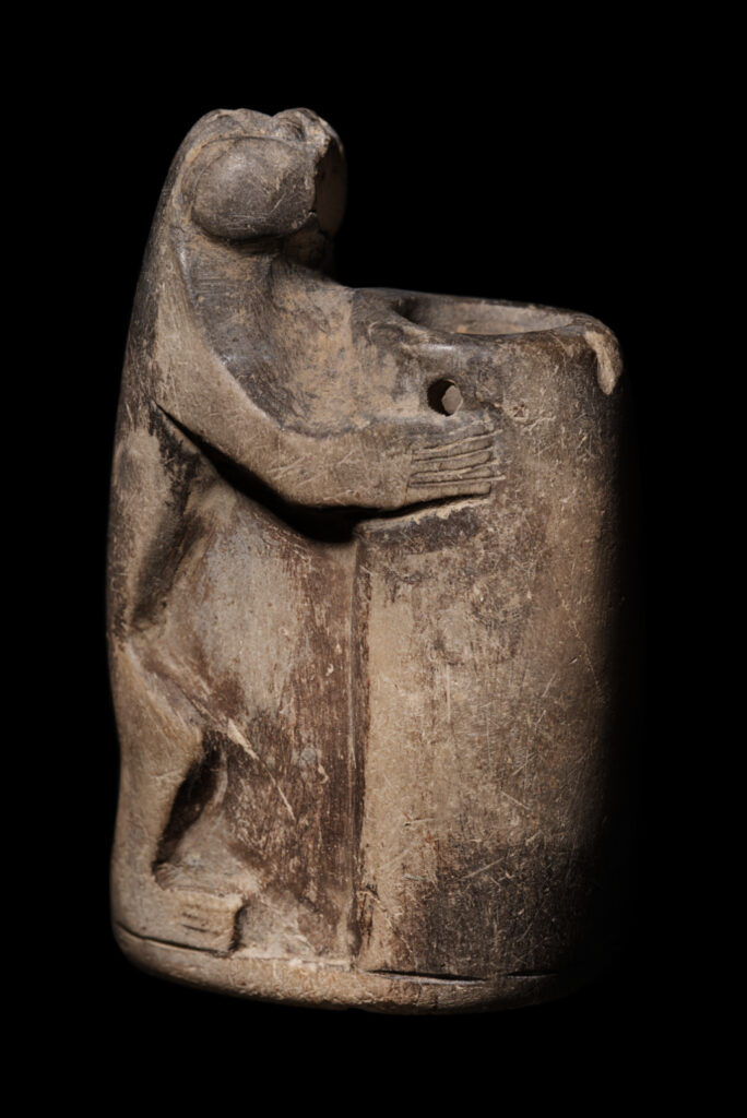 An ancient Egyptian small, tubular pot held by a standing baboon.