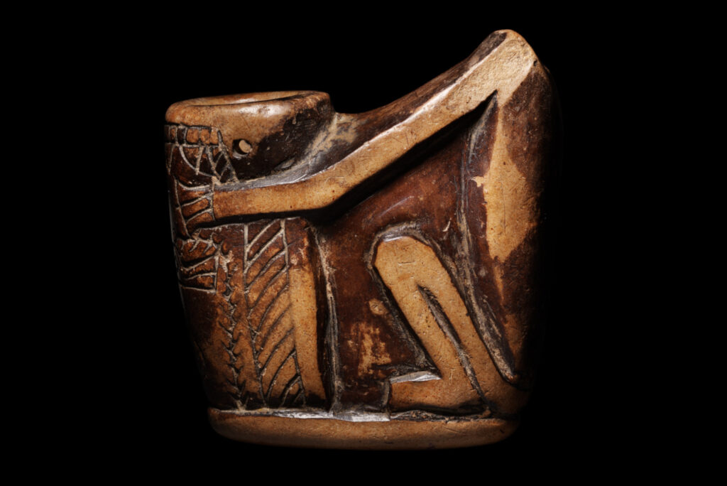 An ancient Egyptian small, tubular pot held by a seated baboon.