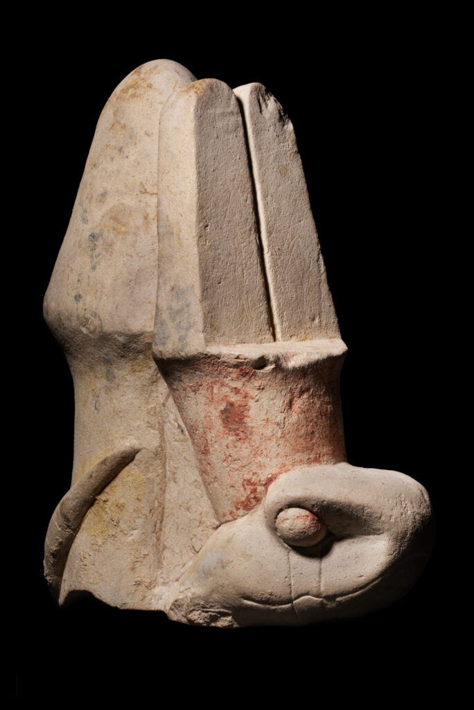 A fragment of a limestone statue showing the head of a cobra wearing the red crown of Egypt topped by two tall, plumed feathers.