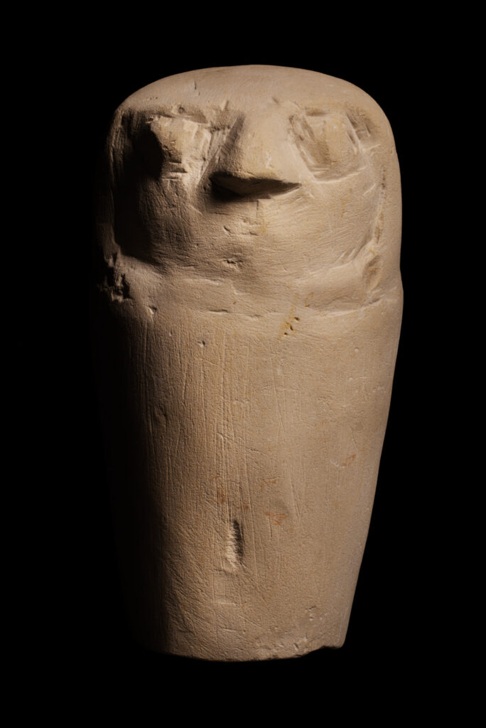 An ancient Egyptian limestone statuette with a falcon head with a plain, undecorated tube-shaped body made to look like a Canopic jar.