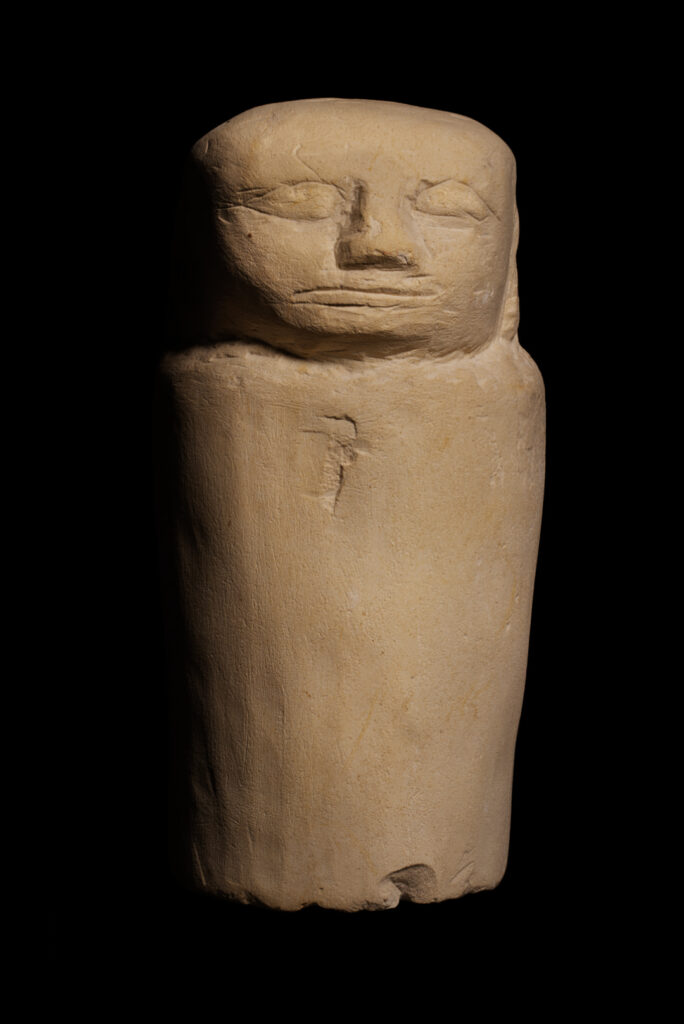 An ancient Egyptian limestone statuette with a human head with a plain, undecorated tube-shaped body made to look like a Canopic jar.