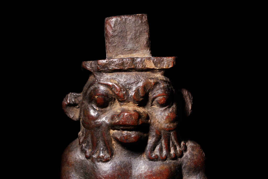 A close-up of the face of a wooden statuette of Bes.