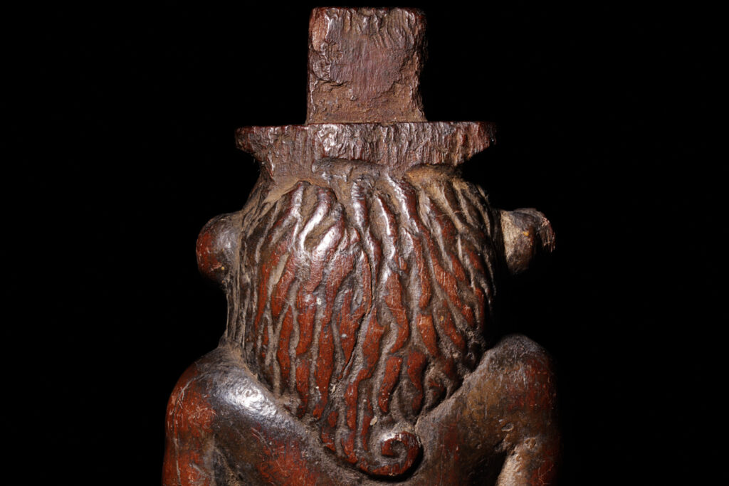 A close-up of the back of the head of a wooden statuette of Bes, showing the mane.