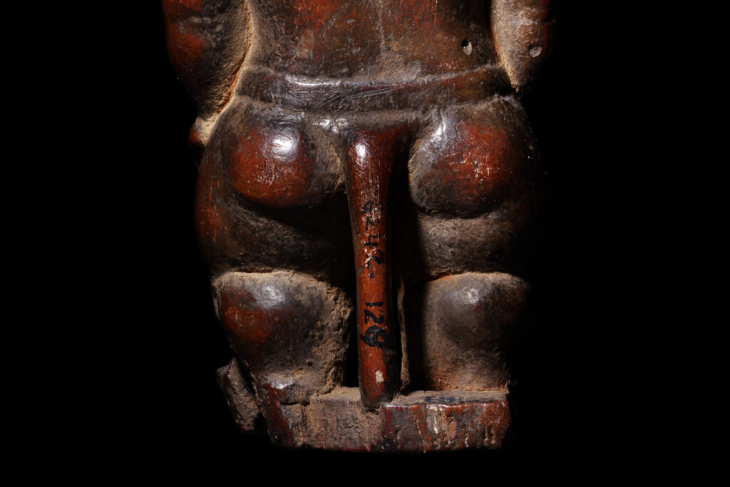 A close-up of the tail and back of the lower half of a wooden statuette of Bes.