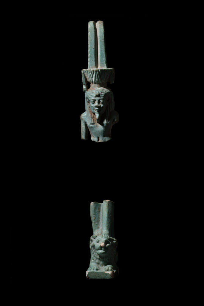 An ancient Egyptian amulet of Nefertem - a male human god with a headdress of tall feathers atop a lotus flower, standing on a recumbant lion. The amulet is missing the mid section between his stomach and knees.