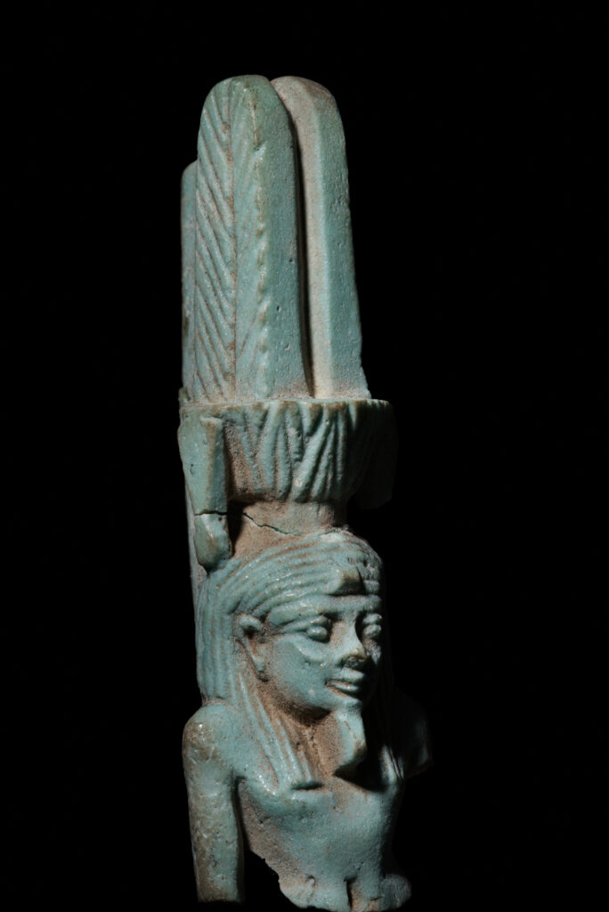 The head from an ancient Egyptian amulet of Nefertem - a male human god with a headdress of tall feathers atop a lotus flower.