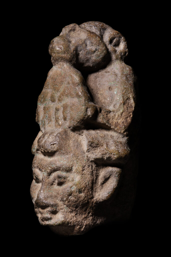 The head from a figurine of a man with a baboon at the back of his head.