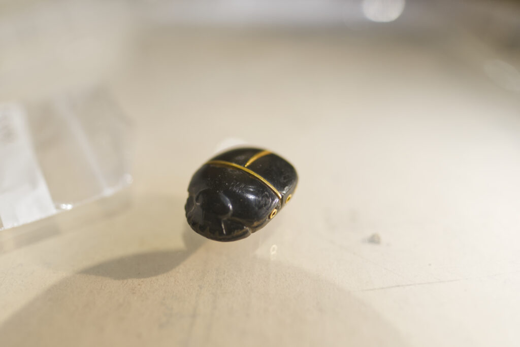 A small, black Egyptian scarab amulet with gold banding on its back and sides.