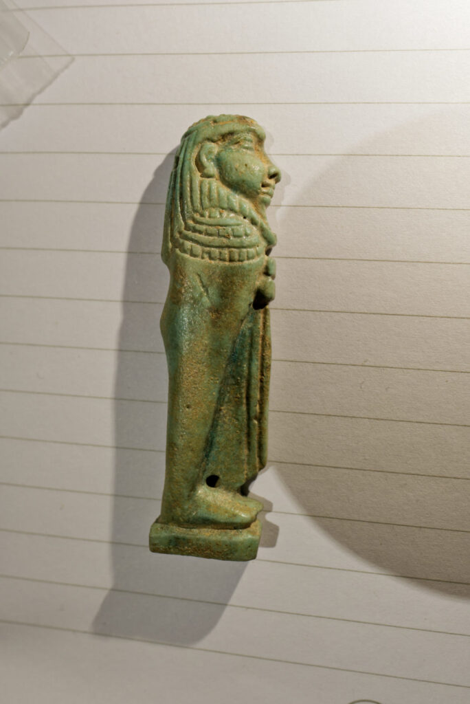 A small faience Egyptian amulet of a mummiform man shown in profile.