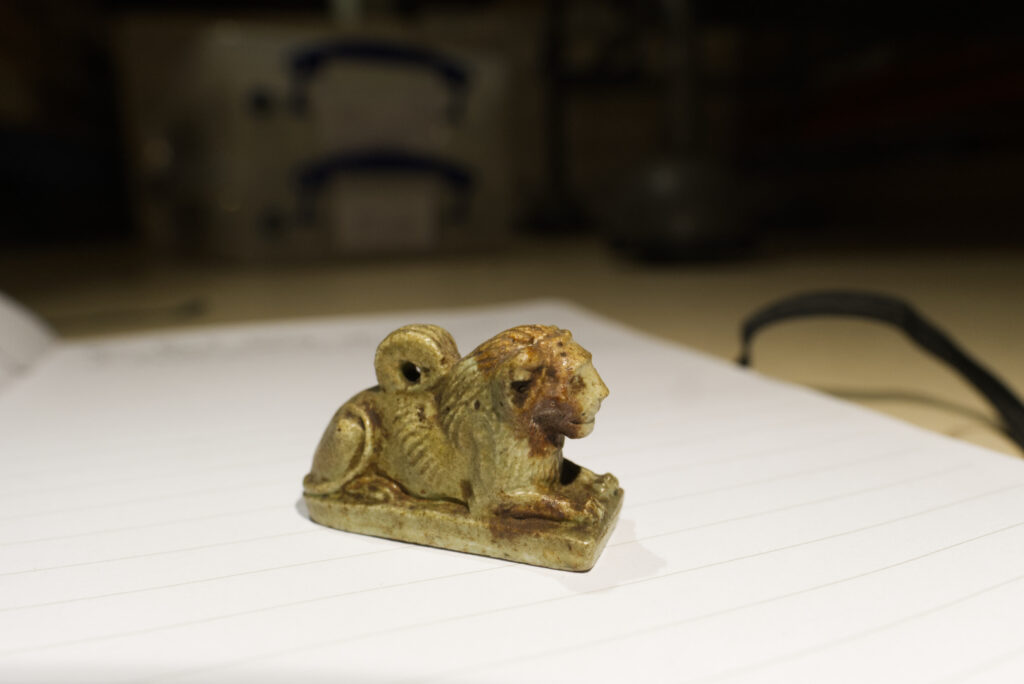 A small faience Egyptian amulet of a recumbent male lion.