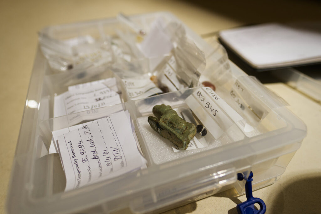 A shallow plastic storage box, open, showing small plastic bags holding ancient Egyptian amulets.