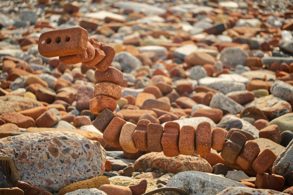 A sculpture made by threading old bricks onto a piece of thick metal wire sticking out from a piece of old building rubble. It looks like a snake rearing up.