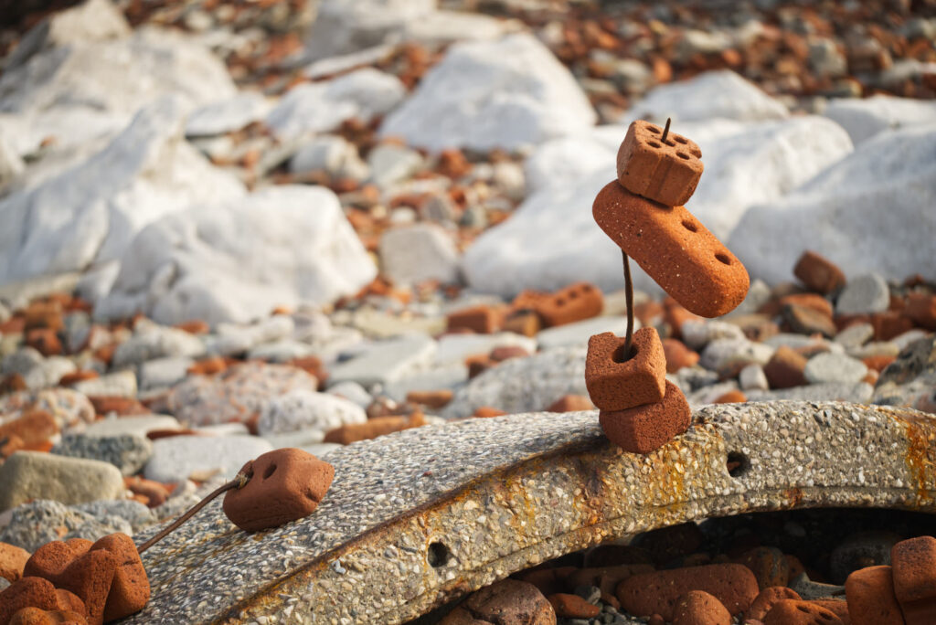 Three old bricks threaded onto a piece of thick metal wire sticking out of a piece of old building concrete on the beach.